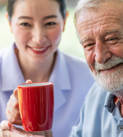 Älterer Herr und Krankenpflegerin halten eine Tasse Kaffee in den Händen.