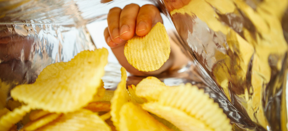 Person greift in eine Chips-Tüte.