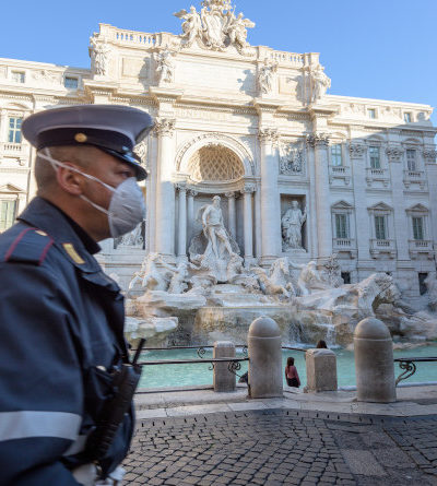 Polizist mit Mundschutz läuft über verlassenen Platz des Trevi-Brunnens in Rom, Italien.