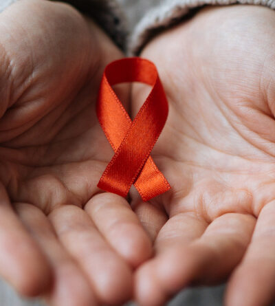Person hält eine rote Schleife, als Zeichen der Solidarität mit HIV-Infizierten, in den Händen.