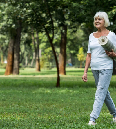 Ältere Frau läuft mit Fitness-Matte durch einen Park