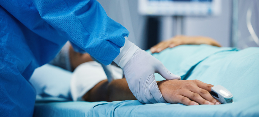 Nahaufnahme eines Arztes, der neben einem Patienten oder einer Patientin steht und in OP-Kleidung die Hand des Patienten oder der Patientin hält.