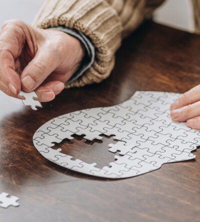 Senior puzzelt ein Puzzle, das einen menschlichen Kopf darstellen soll.