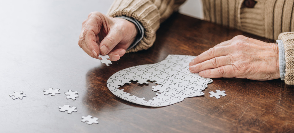 Senior puzzelt ein Puzzle, das einen menschlichen Kopf darstellen soll.