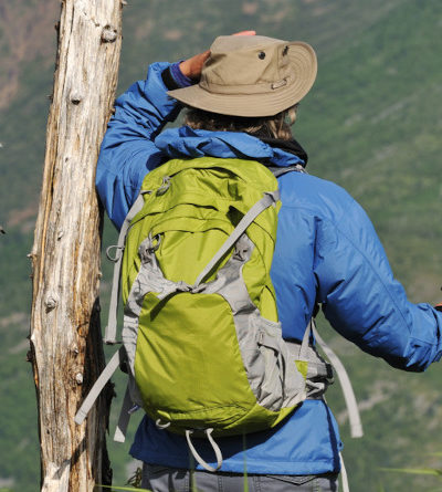 Person mit Outdoor-Jacke und Rucksack steht auf einem Berg und blickt ins Tal.