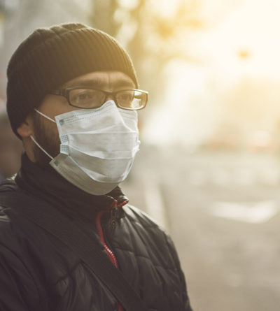 Mann mit einer Atemschutz-Maske steht auf einem Bürgersteig