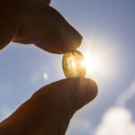 Nahaufnahme. Person hält Vitamin-D-Tablette in der Hand. Im Hintergrund ist der Himmel sichtbar.