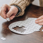 Senior puzzelt ein Puzzle, das einen menschlichen Kopf darstellen soll.